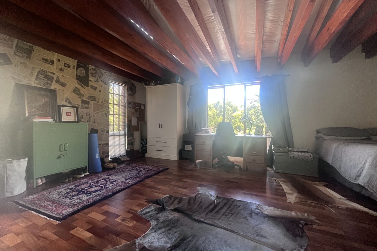 Spacious bedroom featuring exposed timber ceiling beams, rich hardwood parquet flooring, and a built-in wardrobe, offering a warm and character-filled living space.