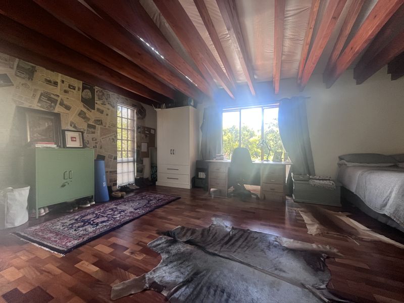Spacious bedroom featuring exposed timber ceiling beams, rich hardwood parquet flooring, and a built-in wardrobe, offering a warm and character-filled living space.