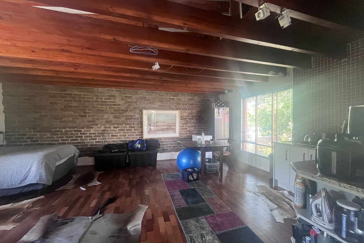 Open-plan living area featuring exposed timber beams, a rustic brick feature wall, hardwood flooring, and a functional kitchen space with granite countertops.