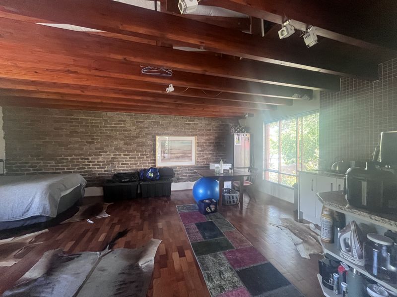 Open-plan living area featuring exposed timber beams, a rustic brick feature wall, hardwood flooring, and a functional kitchen space with granite countertops.