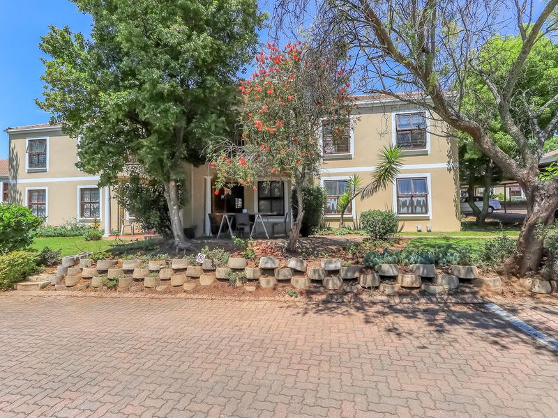 Front elevation of a two-story townhouse featuring a paved driveway, established garden, and a retaining wall with a tiled roof structure.