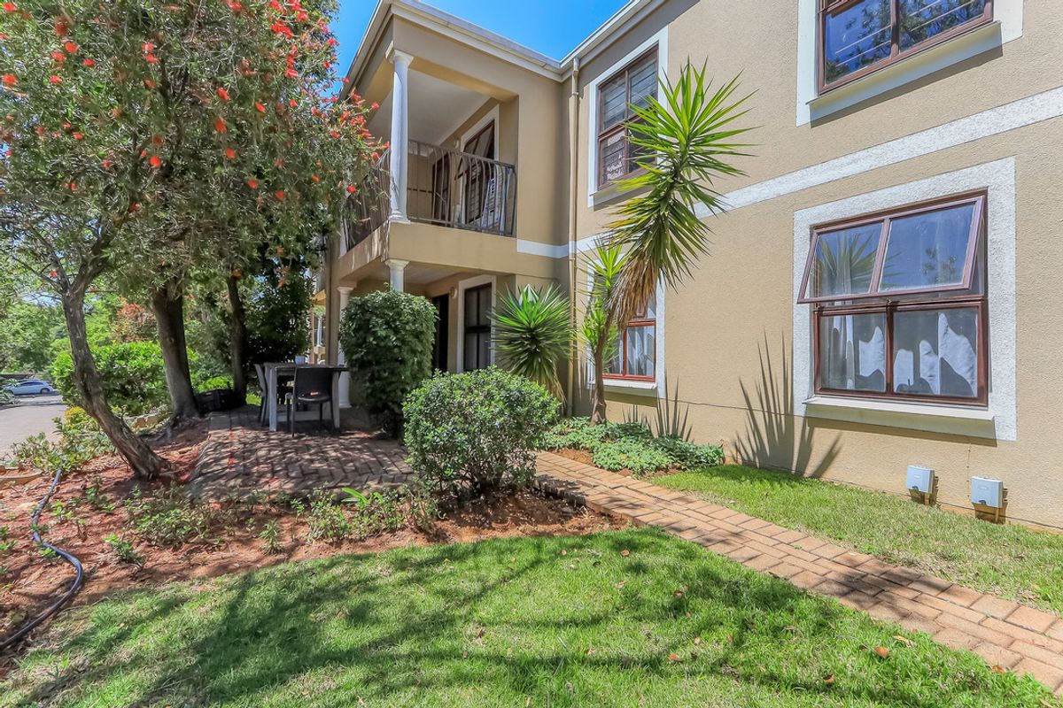 Rear view of the townhouse featuring a brick-paved patio, a covered balcony with wrought iron railings, and well-maintained garden landscaping.