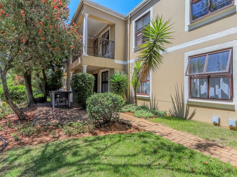 Rear view of the townhouse featuring a brick-paved patio, a covered balcony with wrought iron railings, and well-maintained garden landscaping.