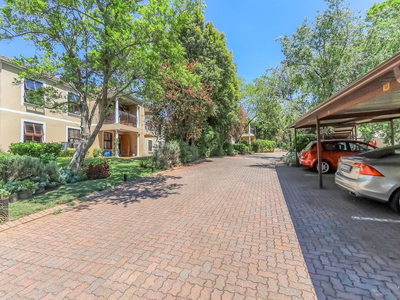 Exterior view of a townhouse complex featuring a paved driveway, covered carport parking, and established garden landscaping.