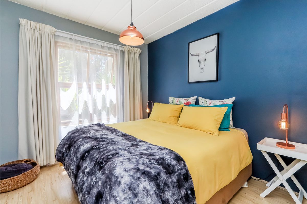 A well-lit bedroom featuring laminate flooring, a feature accent wall, and a large window with curtain tracks.