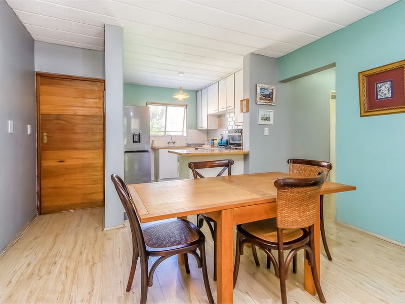Open-plan living and dining area featuring laminate flooring and a functional kitchen with built-in cabinetry and a tiled backsplash.