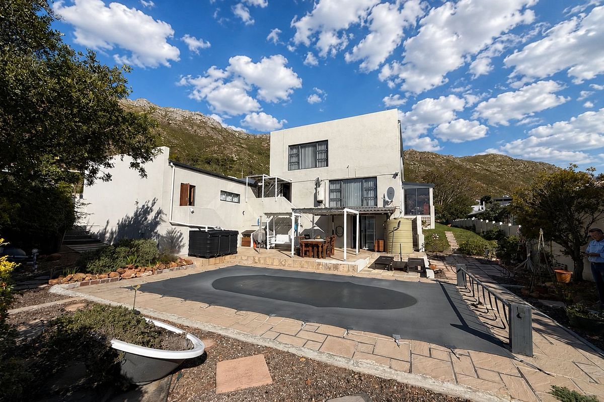 Rear exterior view of the house featuring a paved patio area, swimming pool with cover, and a water tank set against a mountain backdrop.