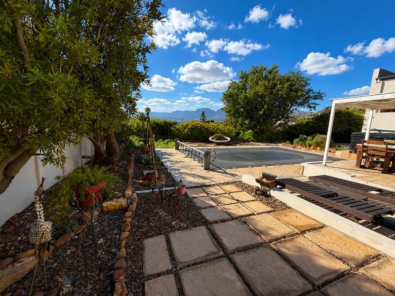 Outdoor pool area featuring a paved patio, pool cover, and pergola, set against a backdrop of mountain views and landscaped garden elements.