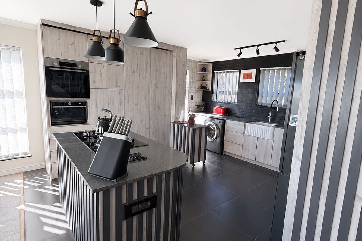 Modern kitchen featuring a central island with hob, built-in appliances, farmhouse sink, and contemporary cabinetry with high-quality finishes and stylish lighting.