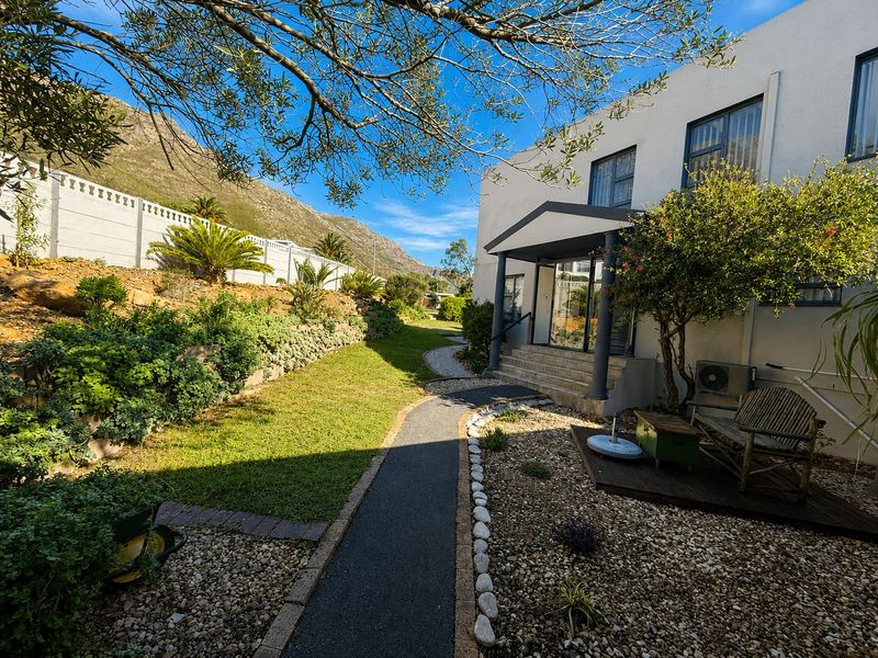 A well-maintained rear garden featuring a paved walkway, landscaped terraced beds, and a covered entrance porch with mountain views.