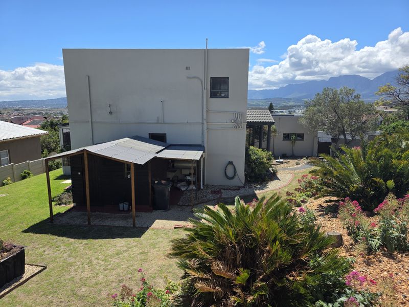 Rear view of the property featuring a covered patio area, landscaped garden, and mountain views in the background.