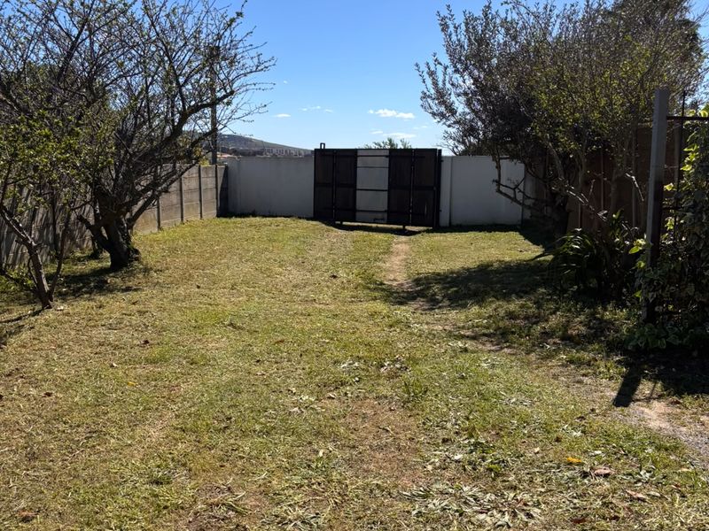 A spacious rear garden featuring a perimeter wall, metal gate access, and mature trees, offering potential for landscaping and outdoor development.