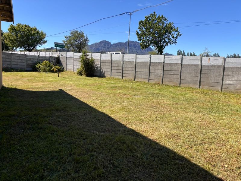 A spacious backyard featuring a well-maintained lawn enclosed by a precast concrete boundary wall with mountain views in the background.