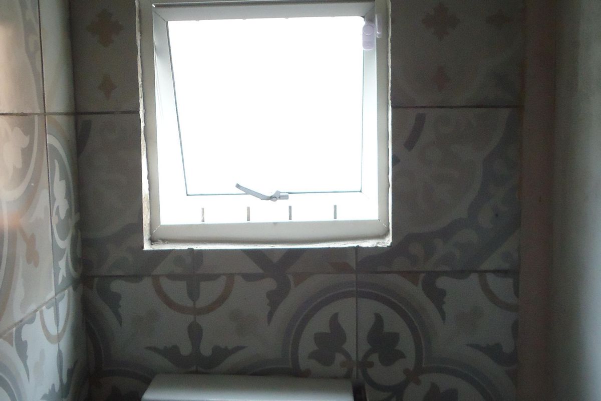 A small bathroom featuring patterned wall tiles and a casement window, currently showing signs of wear and maintenance needs.