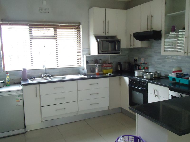 A functional kitchen featuring white cabinetry, dark countertops, a built-in oven with extractor fan, and a tiled backsplash with a window view.