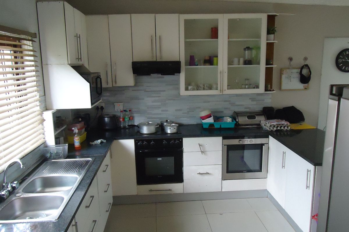 A functional kitchen featuring white cabinetry, dark countertops, a double sink, built-in oven and hob, and tiled flooring with a tiled splashback.