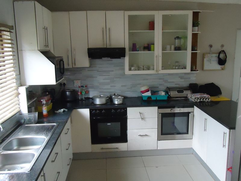 A functional kitchen featuring white cabinetry, dark countertops, a double sink, built-in oven and hob, and tiled flooring with a tiled splashback.