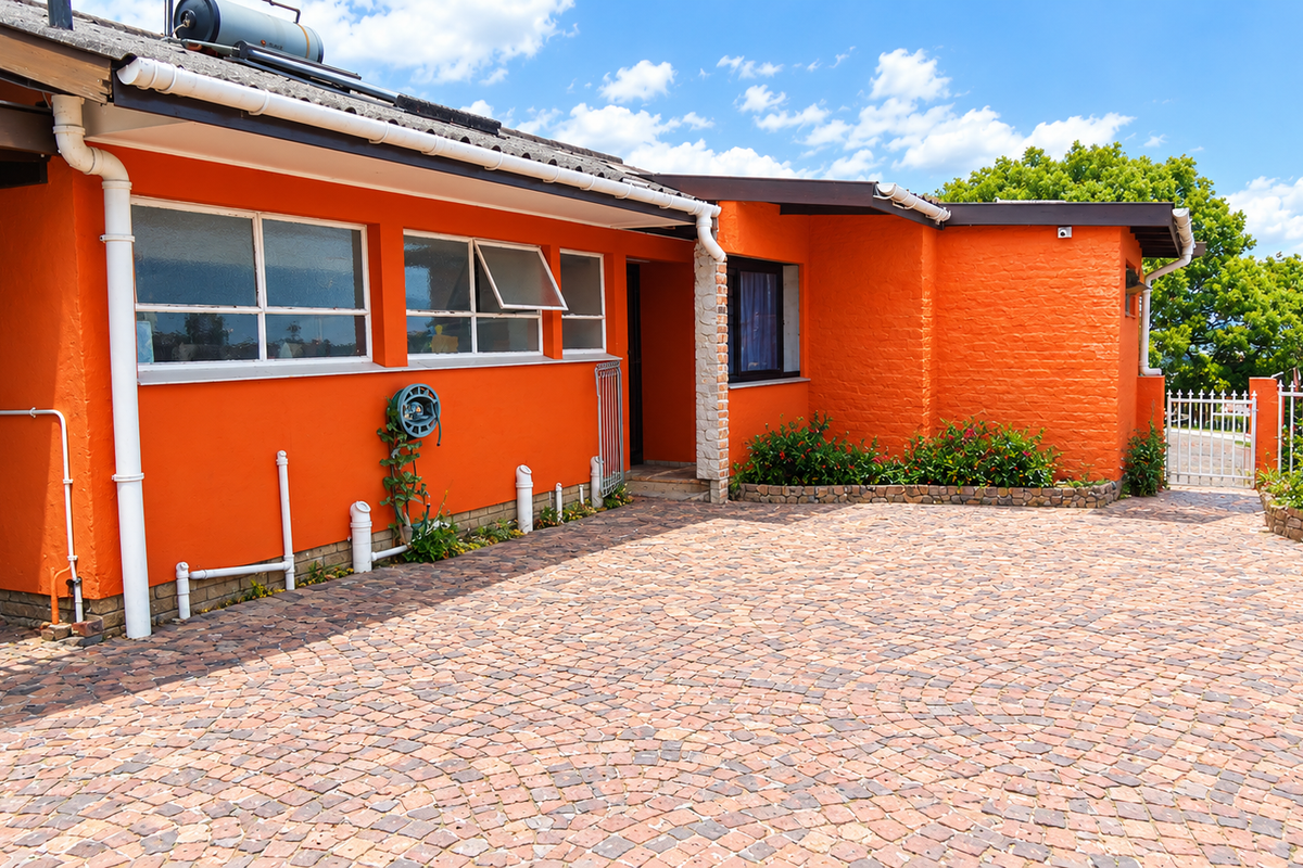 Front exterior view of a house featuring a paved driveway, bright orange brick facade, and functional solar water heating system.