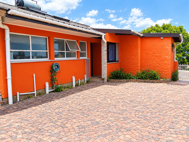 Front exterior view of a house featuring a paved driveway, bright orange brick facade, and functional solar water heating system.