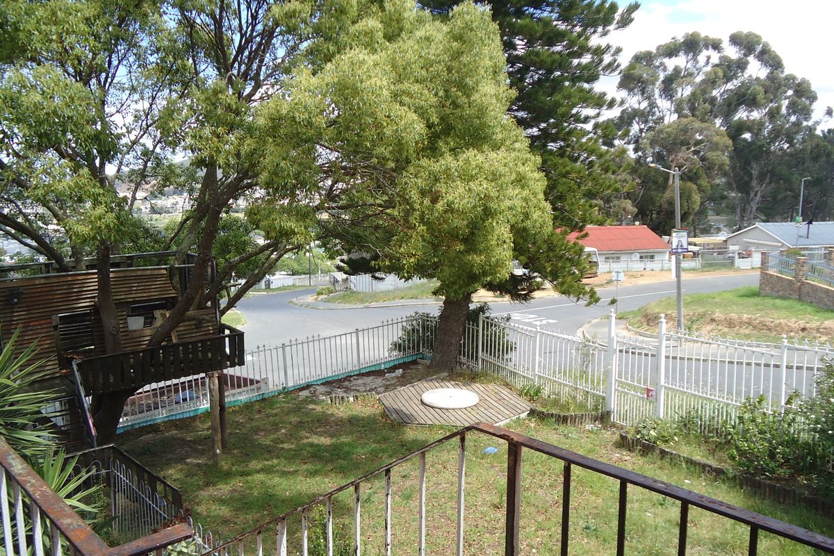 Rear garden area featuring a wooden treehouse, a small deck platform, and metal perimeter fencing overlooking a suburban street corner.