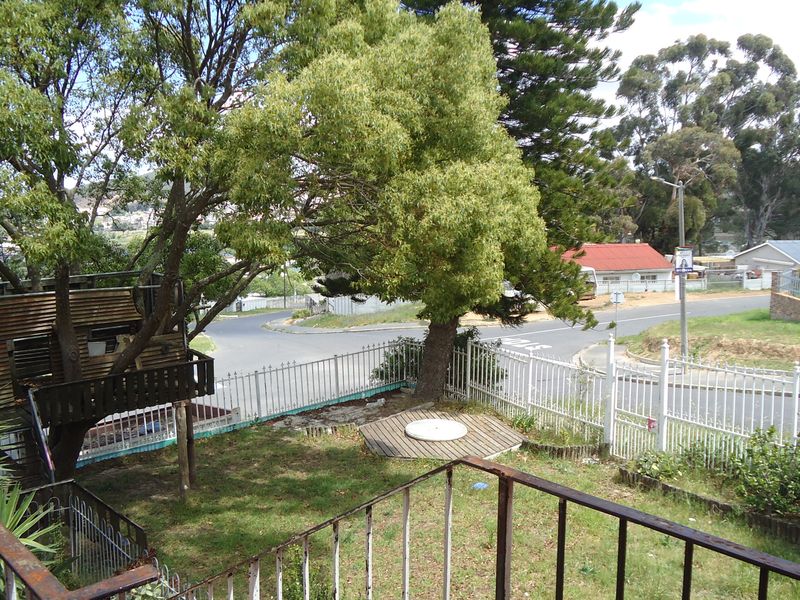Rear garden area featuring a wooden treehouse, a small deck platform, and metal perimeter fencing overlooking a suburban street corner.