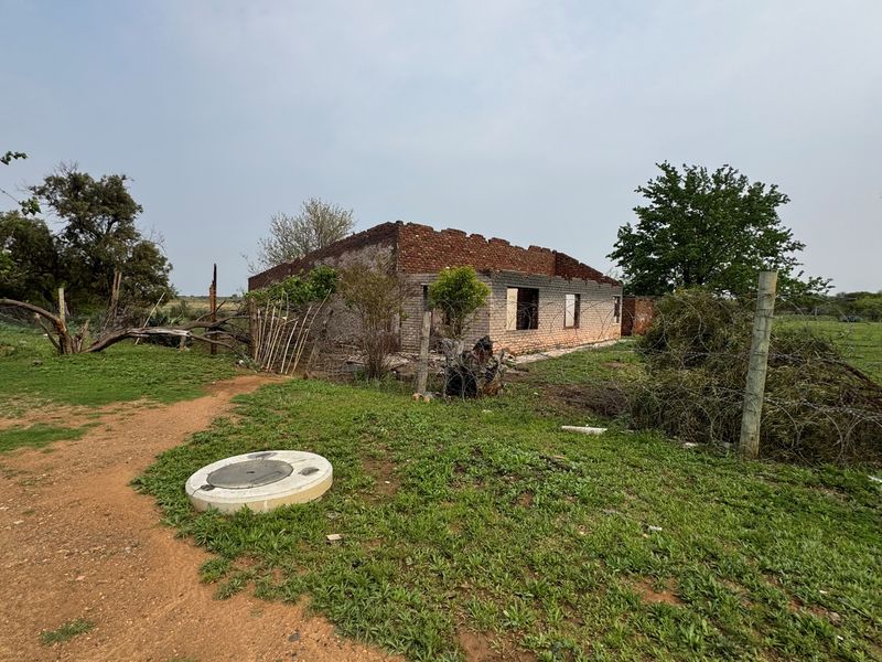 A view of a residential property under construction featuring an incomplete brick structure and surrounding land.