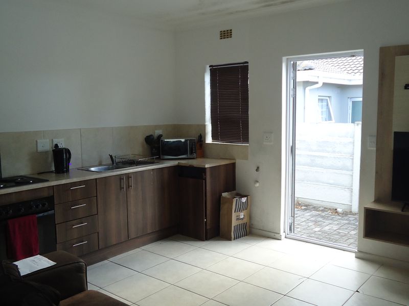 Open-plan living area featuring a compact kitchen with built-in cabinetry, hob, and oven, tiled flooring, and direct access to an outdoor paved area.