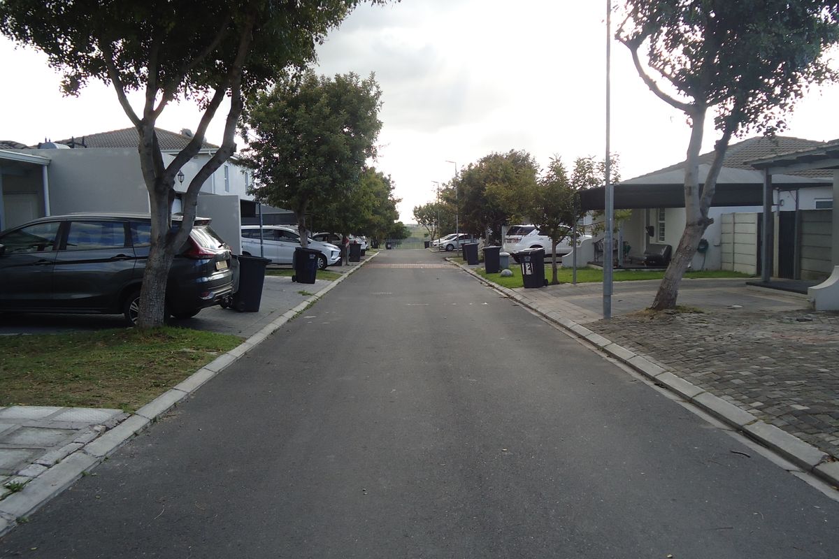 A view of the residential street showing paved road, concrete kerbing, and surrounding housing units with driveways.
