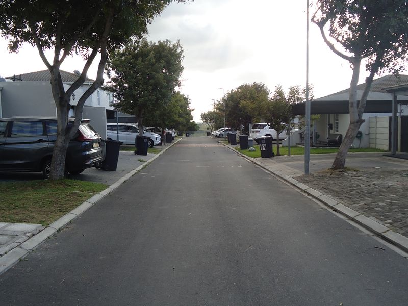A view of the residential street showing paved road, concrete kerbing, and surrounding housing units with driveways.