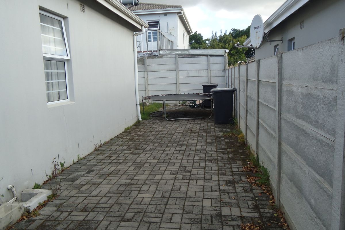 A paved rear exterior area enclosed by precast concrete boundary walls, featuring a side access path along the main building structure.