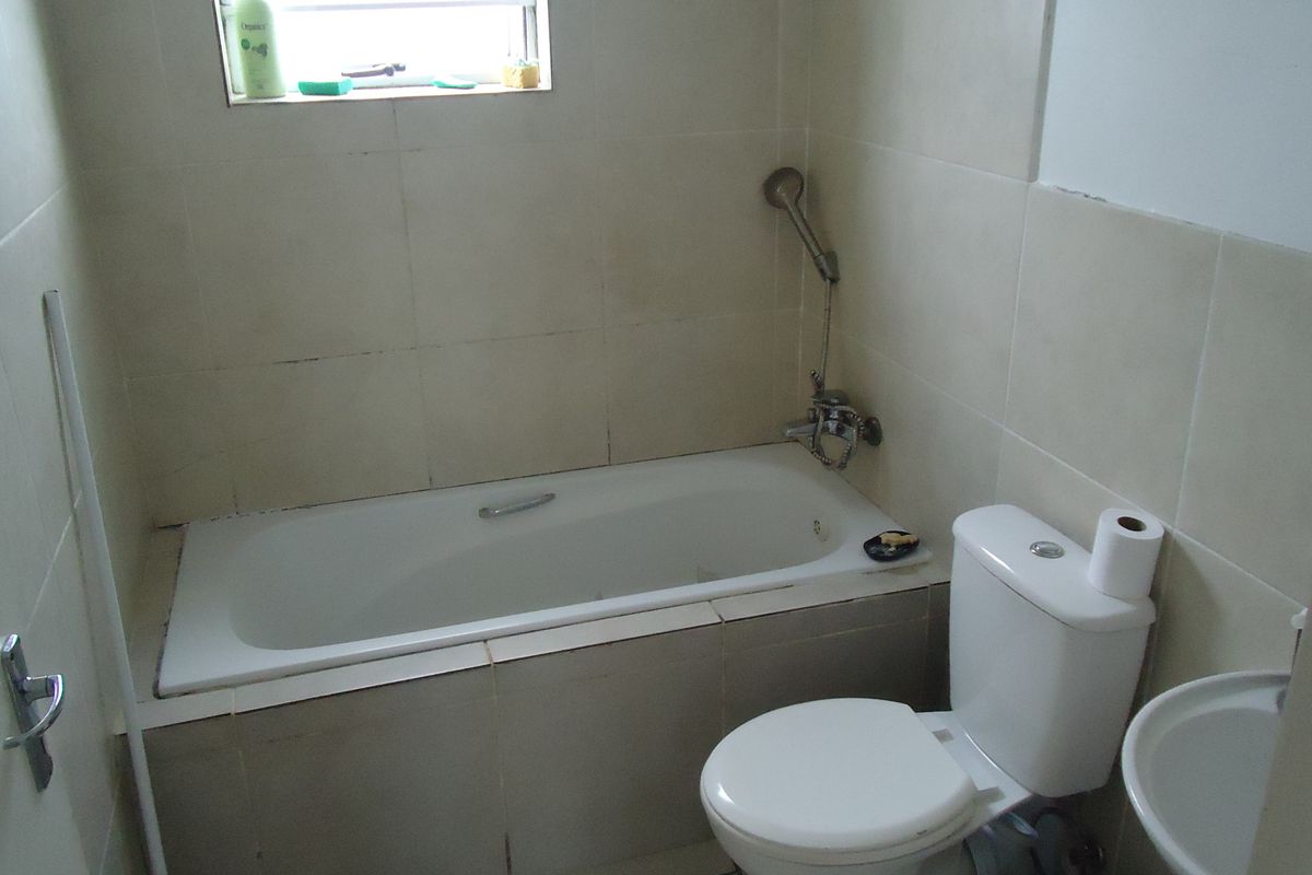 A compact bathroom featuring a built-in bathtub with shower mixer, a standard toilet, and a pedestal sink with neutral wall tiling.