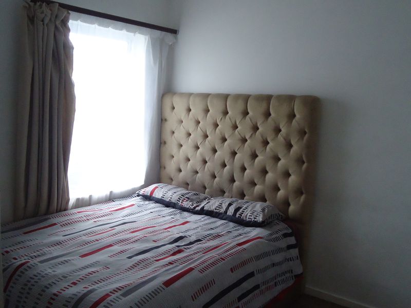A compact bedroom featuring a tufted headboard and window with curtains, providing a simple and functional sleeping space.