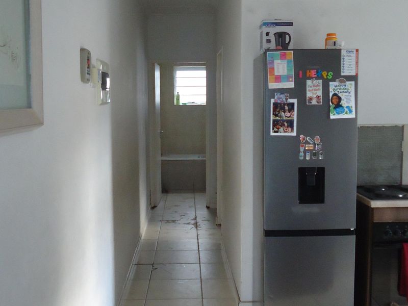 A narrow hallway with tiled flooring leading towards a bathroom, showing signs of wear and requiring cosmetic updates.