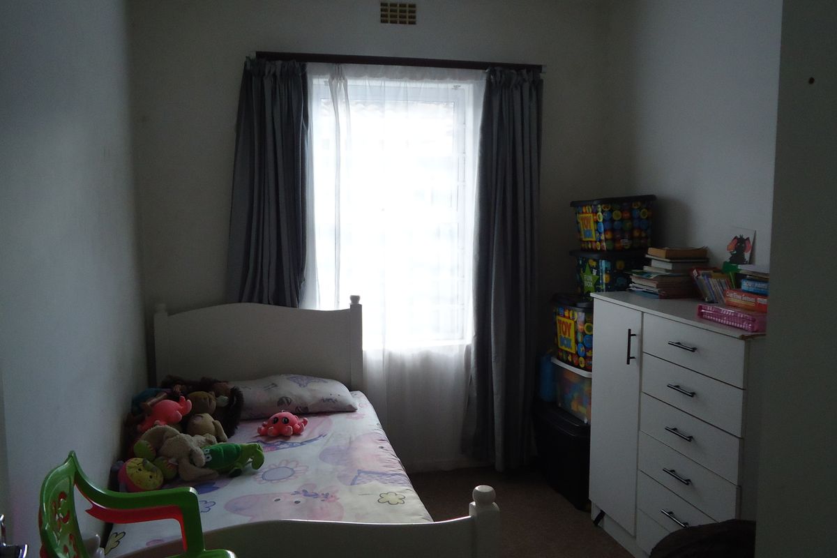A standard bedroom featuring a window with curtains and a ventilation grille, providing a functional space for rest.