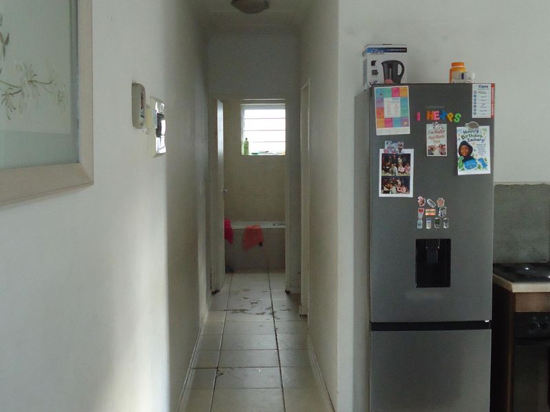 A narrow hallway with tiled flooring leading towards a bathroom, showing signs of wear and requiring cosmetic updates.