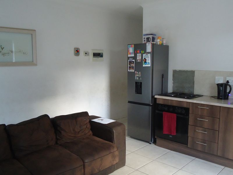 Open-plan living area featuring a compact kitchen with built-in cabinetry, oven, hob, and tiled flooring, suitable for modern living.