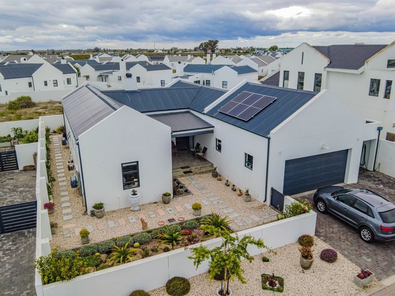 Aerial view of a modern residential property featuring a metal roof with integrated solar panels, a paved driveway, and a well-maintained landscaped garden.
