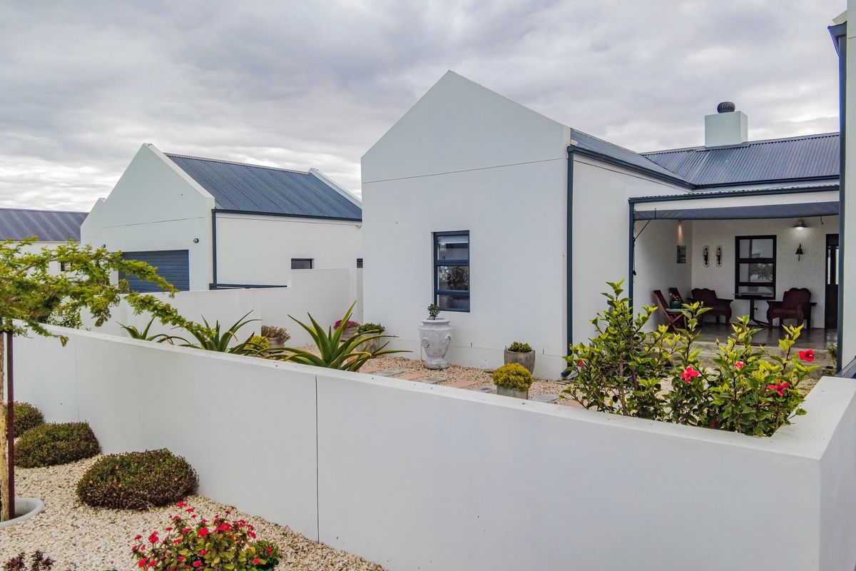 A well-maintained rear exterior view featuring a modern white facade, corrugated metal roofing, a covered patio area, and landscaped gravel garden beds.