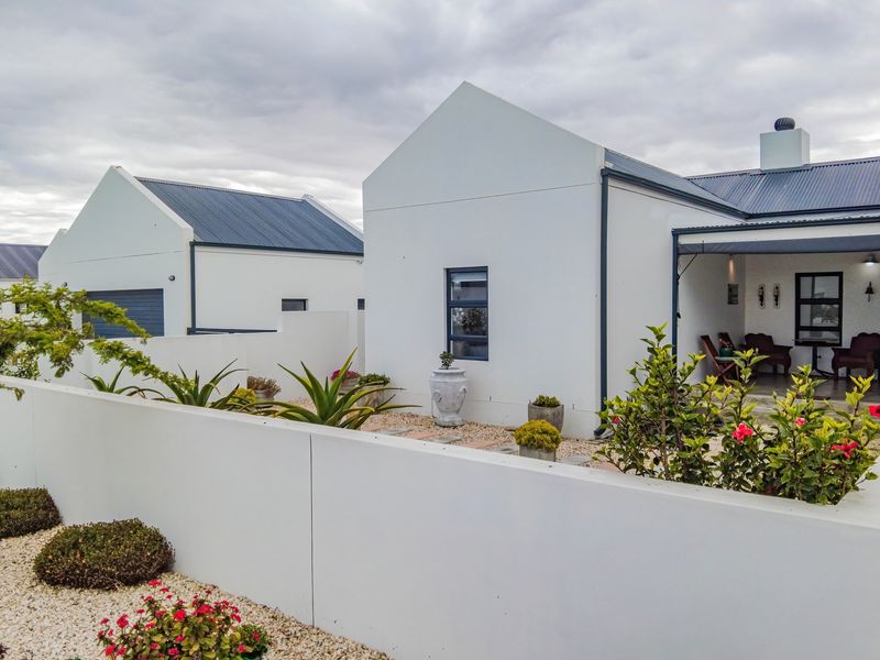 A well-maintained rear exterior view featuring a modern white facade, corrugated metal roofing, a covered patio area, and landscaped gravel garden beds.