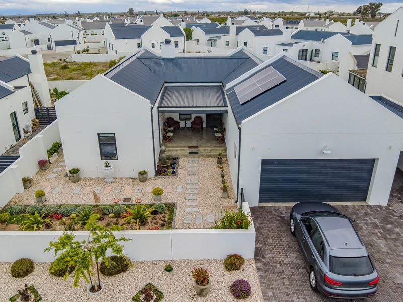 Aerial view of a modern house featuring a metal roof with solar panels, a paved driveway, a covered patio, and a well-maintained landscaped garden.