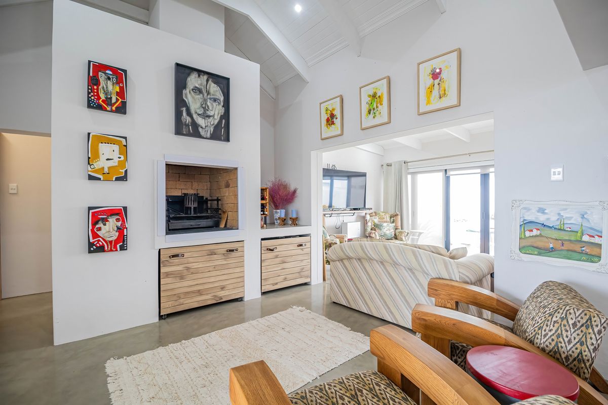 Spacious living room featuring a vaulted ceiling, polished concrete floors, and a prominent built-in fireplace, with seamless flow to an adjacent sunlit area.