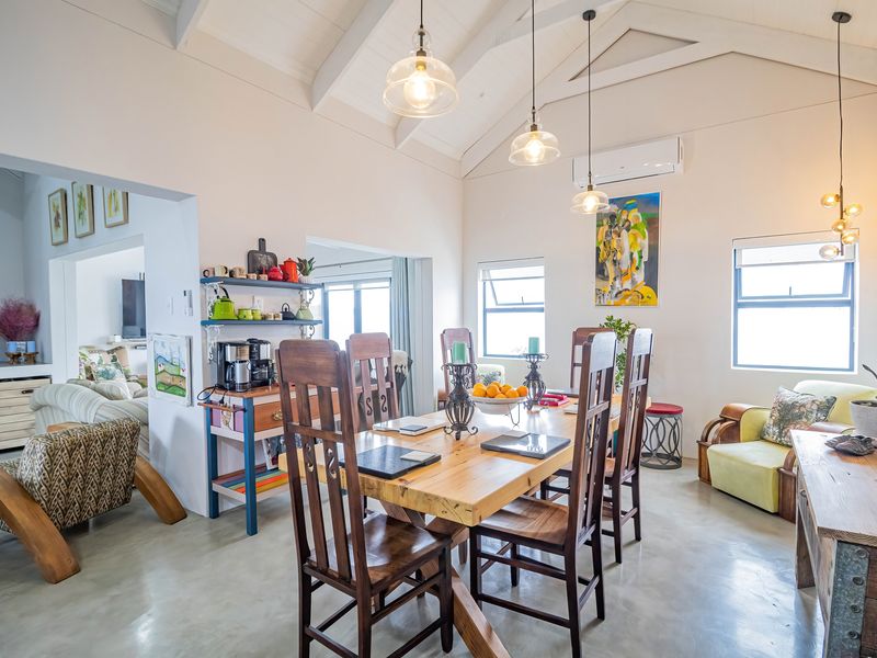 Spacious open-plan dining area featuring high vaulted ceilings with exposed rafters, polished concrete floors, and modern pendant lighting, creating a bright and airy atmosphere.