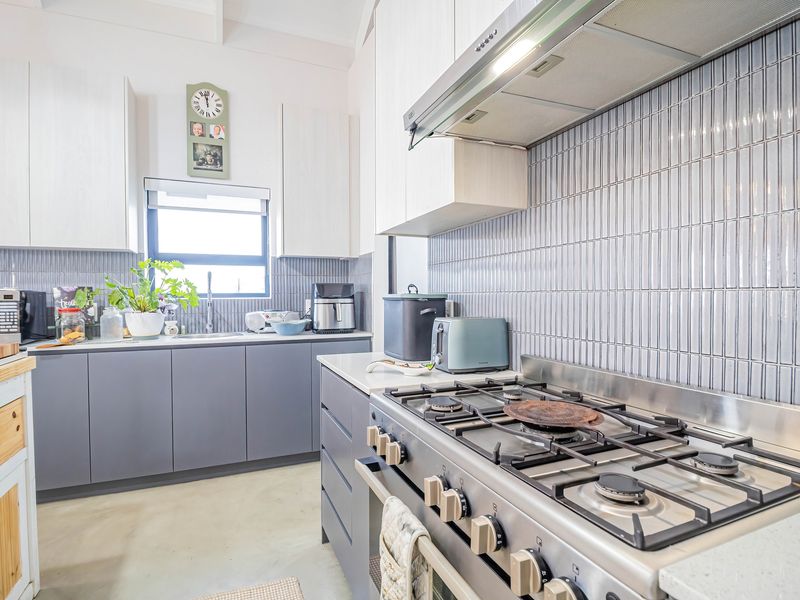 Modern kitchen featuring grey cabinetry, stone countertops, a gas cooktop with extractor fan, and a stylish vertical tile backsplash.