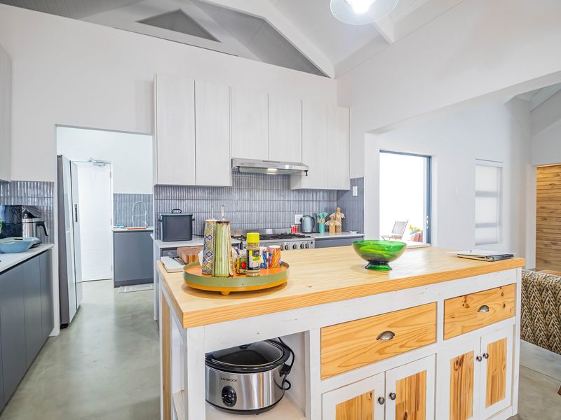 Modern open-plan kitchen featuring a central timber-topped island, sleek cabinetry, vaulted ceilings, and a functional scullery area with contemporary finishes.