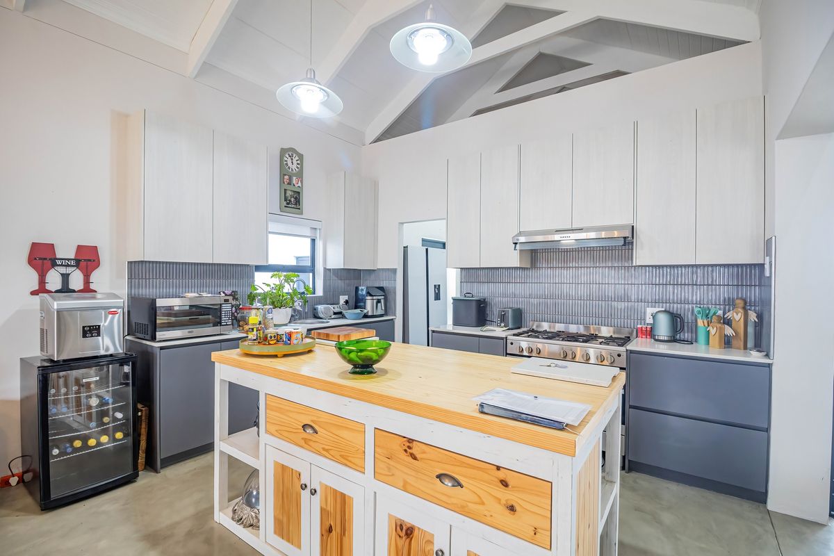 Modern kitchen featuring a central wooden island, gas cooktop with extractor, sleek cabinetry, tiled backsplash, and a spacious vaulted ceiling with pendant lighting.