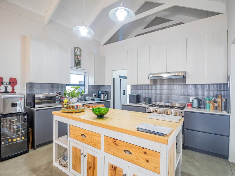 Modern kitchen featuring a central wooden island, gas cooktop with extractor, sleek cabinetry, tiled backsplash, and a spacious vaulted ceiling with pendant lighting.