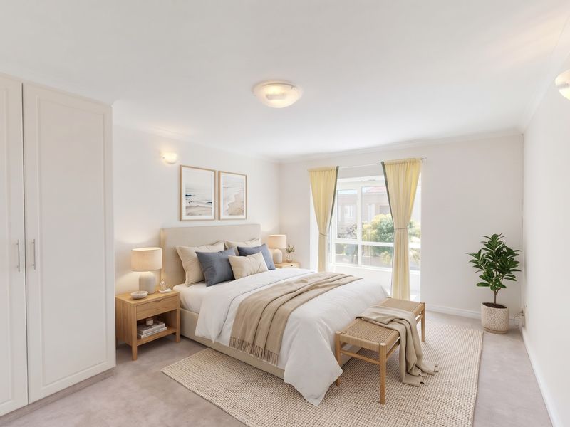 A bright and well-maintained bedroom featuring a built-in wardrobe, neutral carpeting, and a large window allowing for ample natural light.