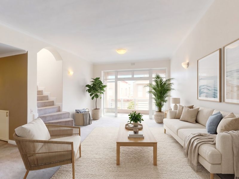 A bright and spacious living room featuring neutral carpeting, an elegant archway leading to a staircase, and large sliding doors providing natural light.