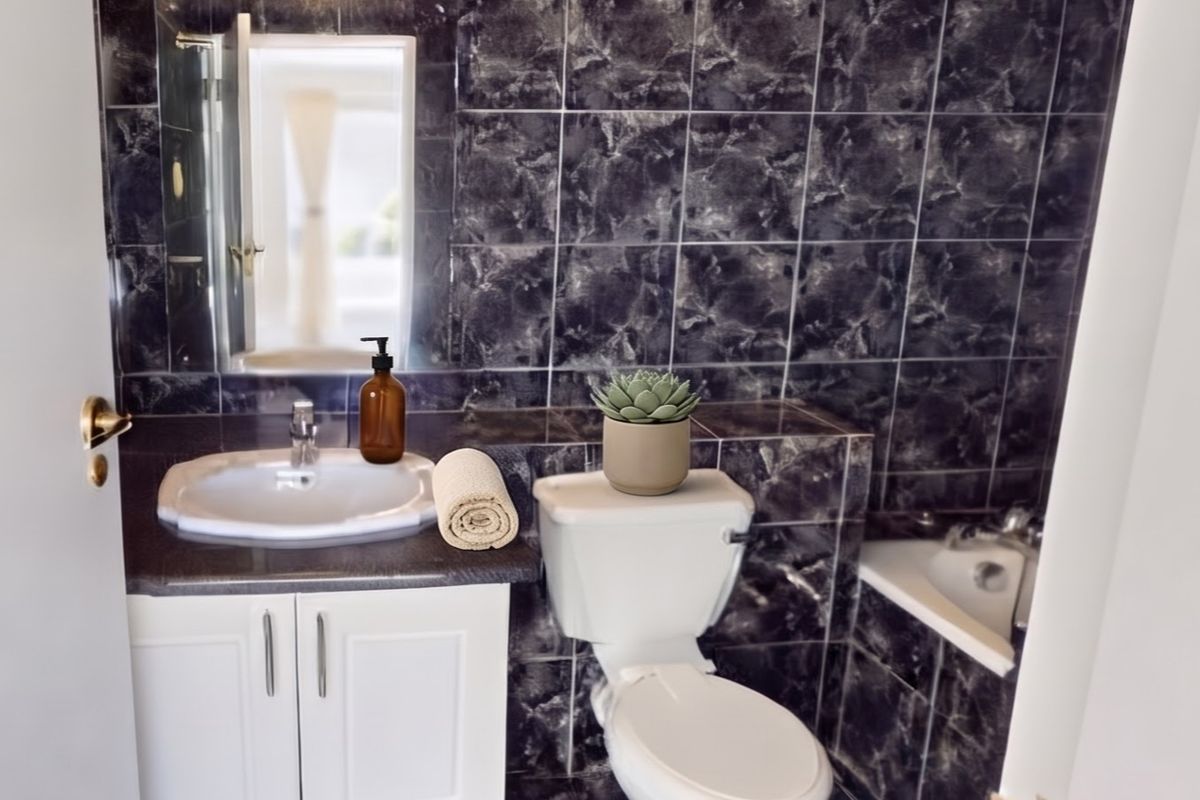 A compact bathroom featuring dark marble-effect wall and floor tiles, a white vanity cabinet with integrated sink, a toilet, and a built-in bathtub.