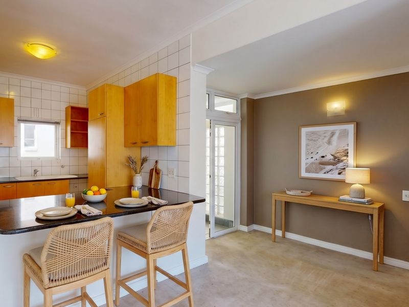 Open plan kitchen and living area featuring wooden cabinetry, a breakfast bar, and neutral wall finishes with access to an external area.